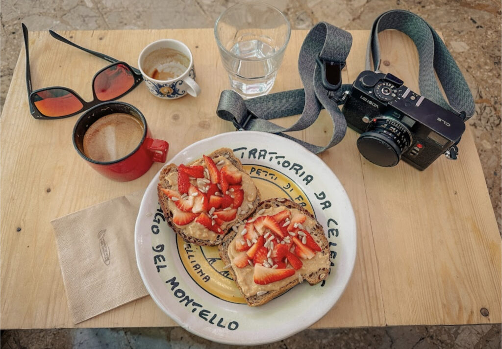 a table at Ammazza Caffé with two cups of coffee, a camera, and some peanut butter toast