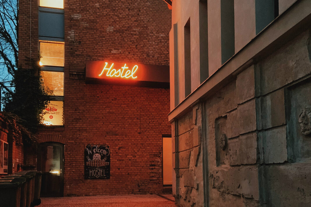 An alley at dusk with a neon sign glowing advertising a hostel