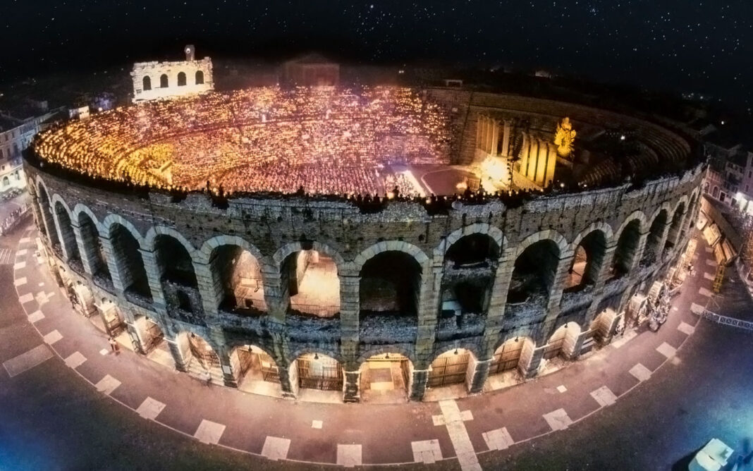 The Verona Arena lit up by lights and a crowd at night